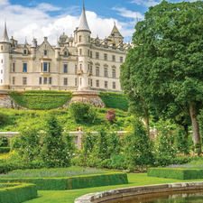 Scottish castle surrounded by lush gardens and trees under a blue sky.